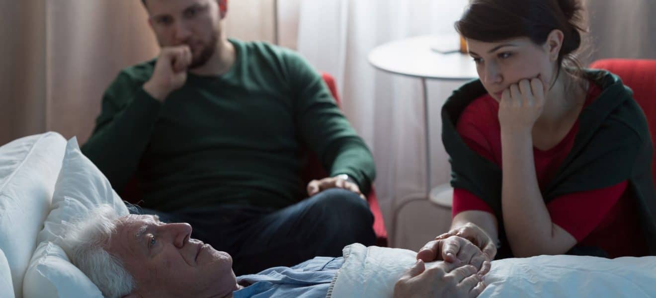 Sorg og diabetes. Mann og kvinne sitter ved sykesengen til gammel mann